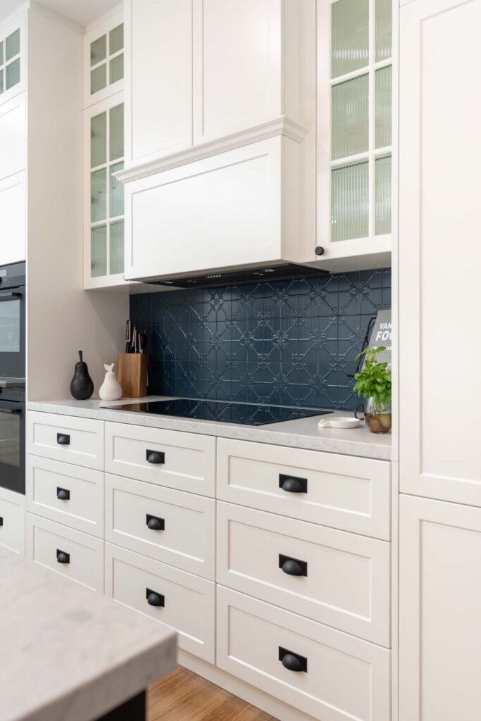 White profile draw units with elegant cabinetry and pressed metal splashback in navy to house the cooking space of the kitchen.