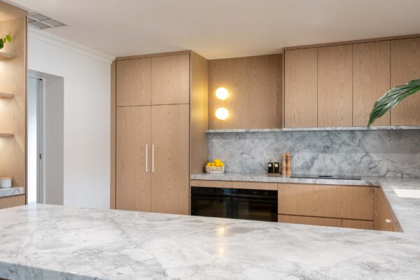 An Organic and delicate blond timber veneer, G shaped kitchen with clean lines and natural marble.