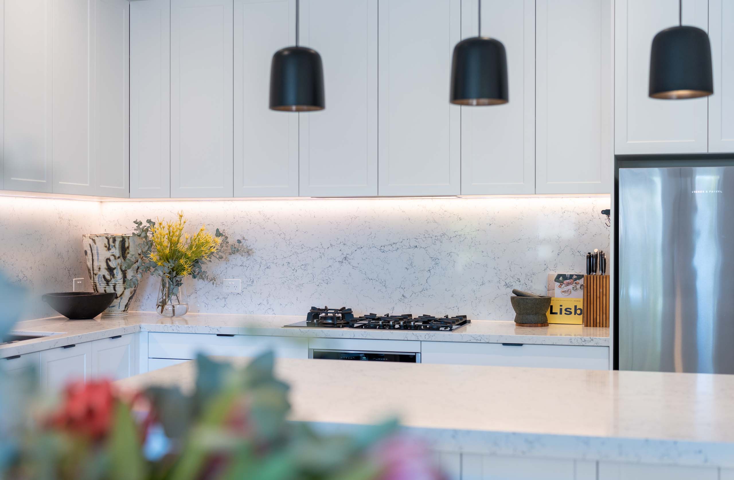 Triple set black industrial pendants work well the black appliances featured in this kitchen space. Colour bursts and clever styling bring it together.