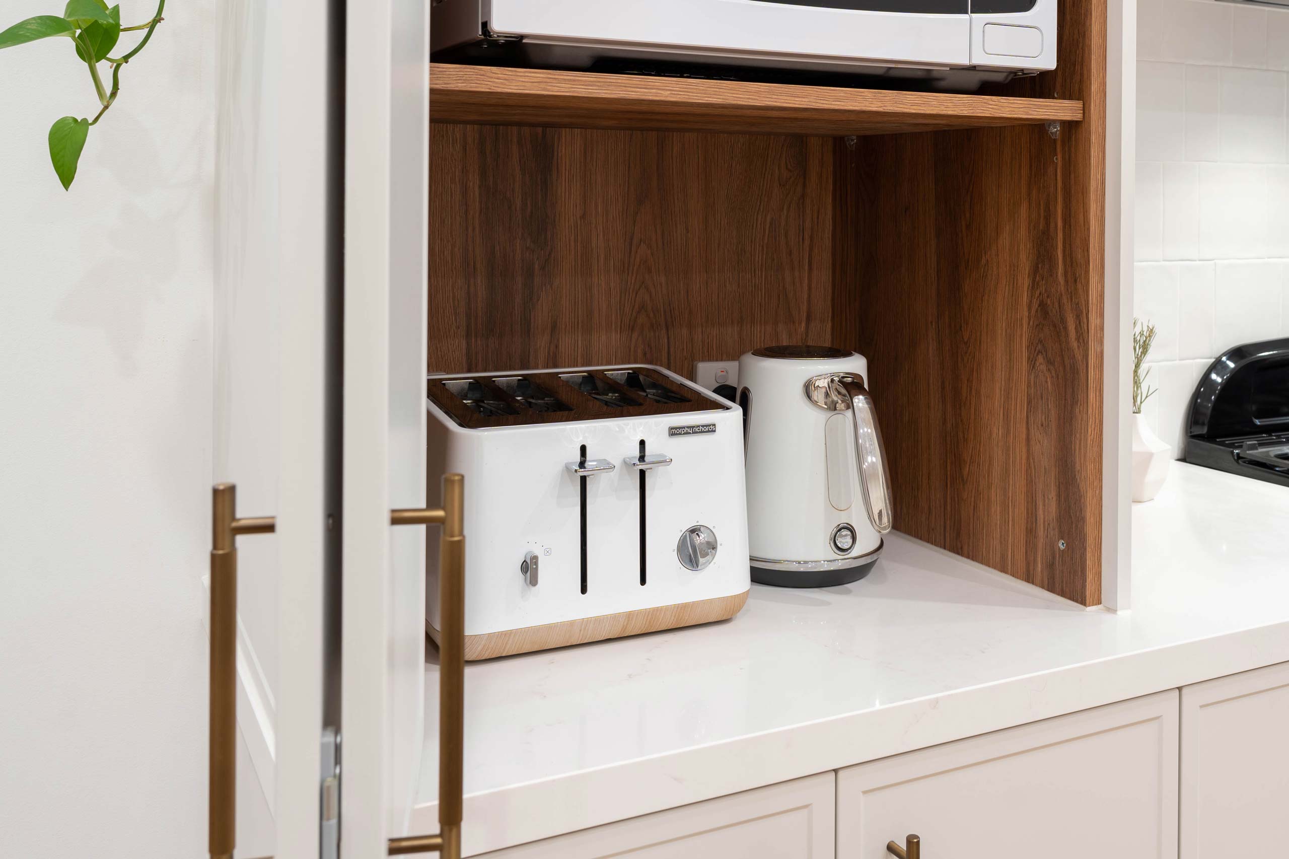 Hidden storage space for microwave, kettle and toaster. White cabinetry with timber internal shelving.