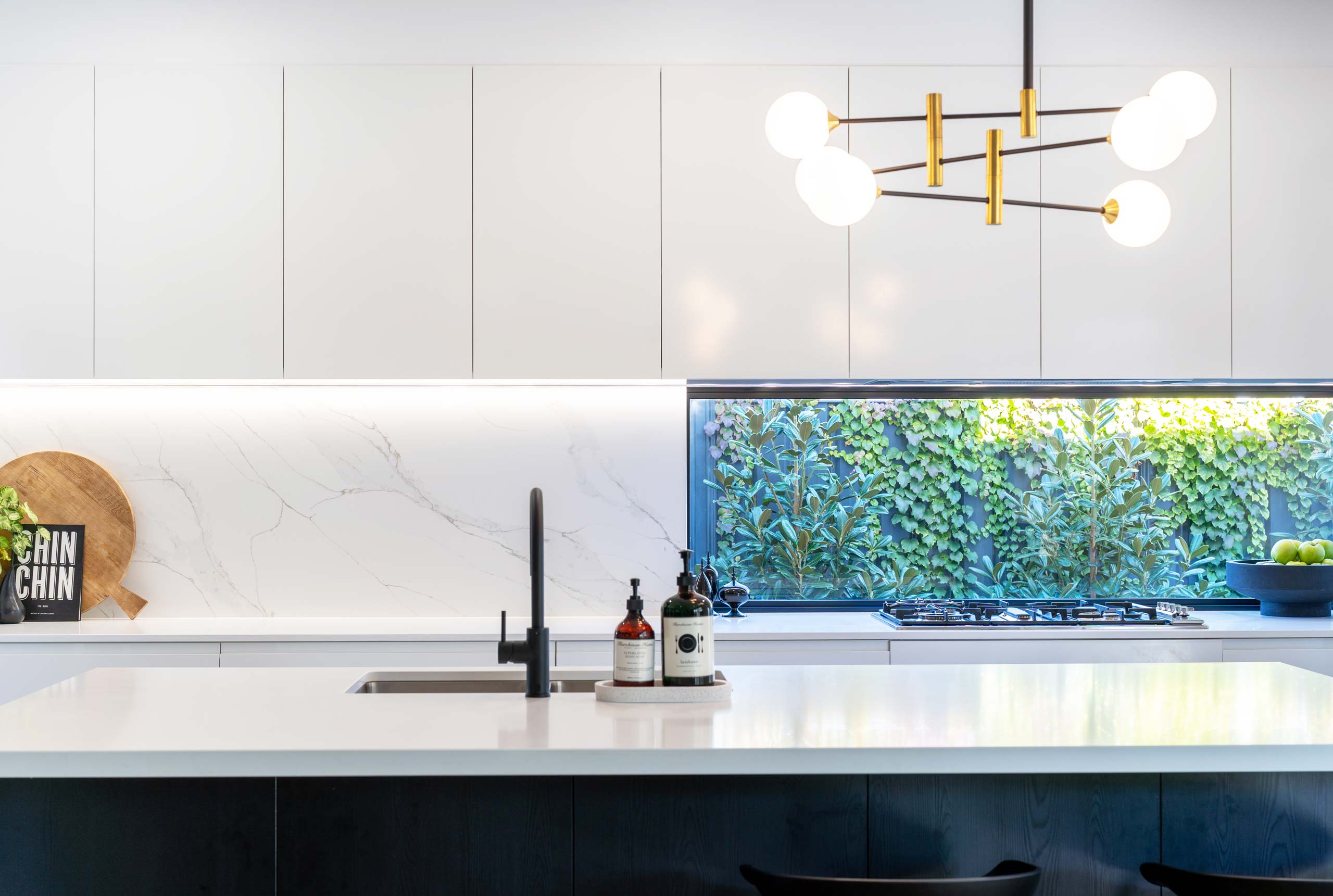 A framed glass splashback brings light into the kitchen highlighting the grey vein stone and the run of white functional overhead cabinetry.