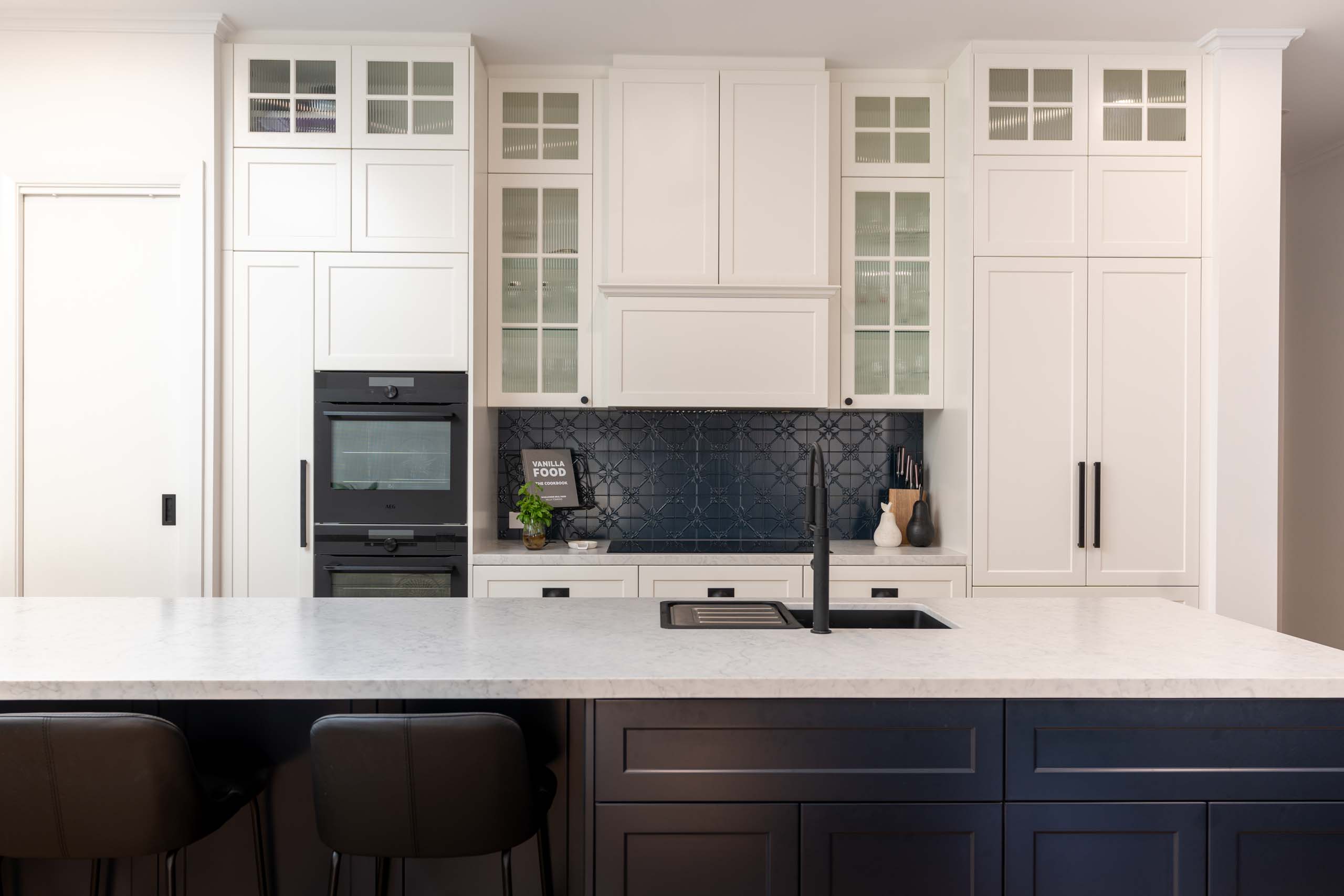 Barossa profile cabinetry in white Linen, pressed metal splashback, Indigo Blue island bar. Glass insert overheads and benchtop with warm grey undertones.