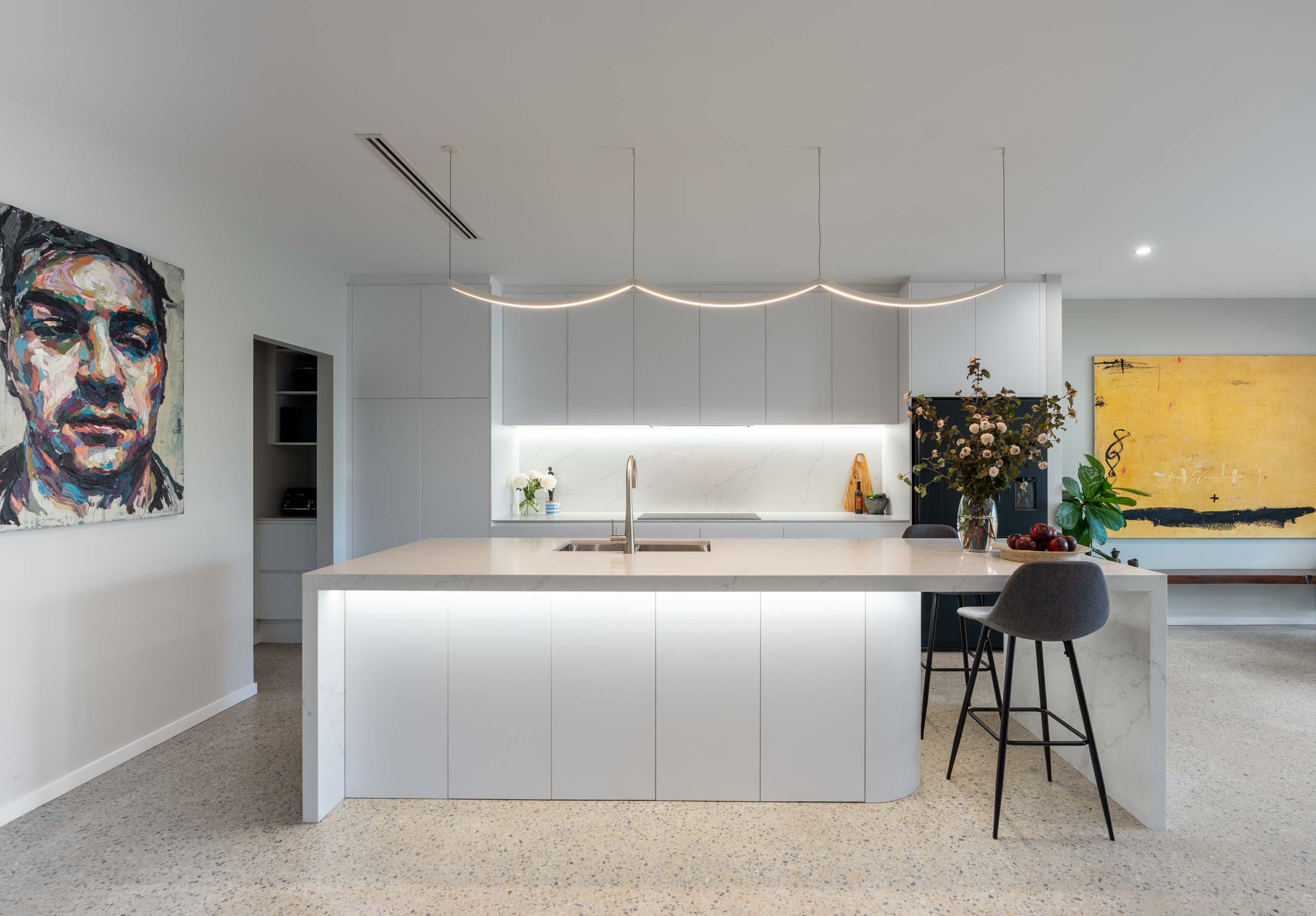 A classic white kitchen with striking black features. Yellow and vibrant colour pop art work with curved under bench cabinetry and polished concrete floor.