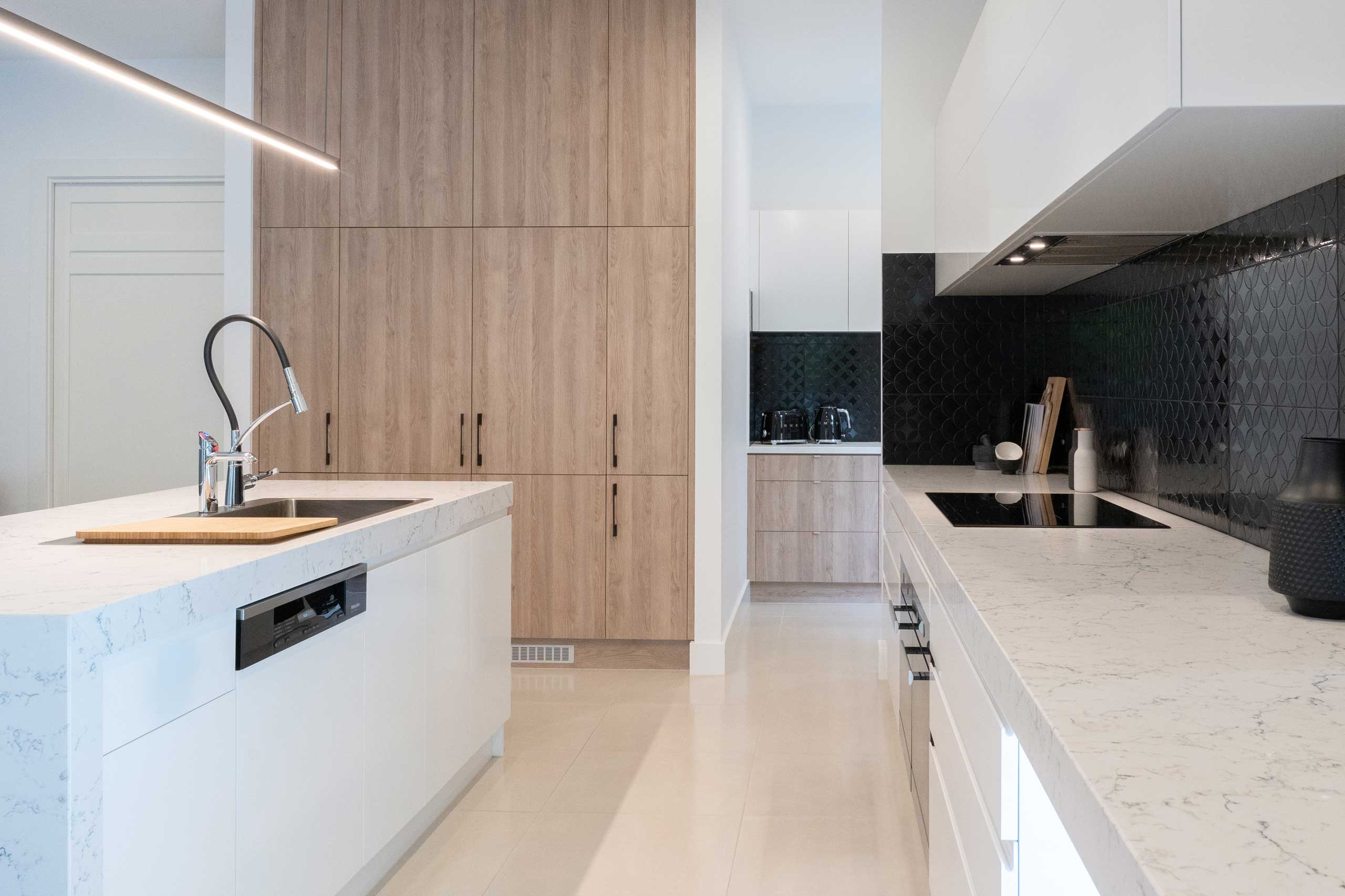 Featured black gloss tiled splashback with a white zenith look benchtop and a timber grain highlight, flowing onto the identical butlers pantry.