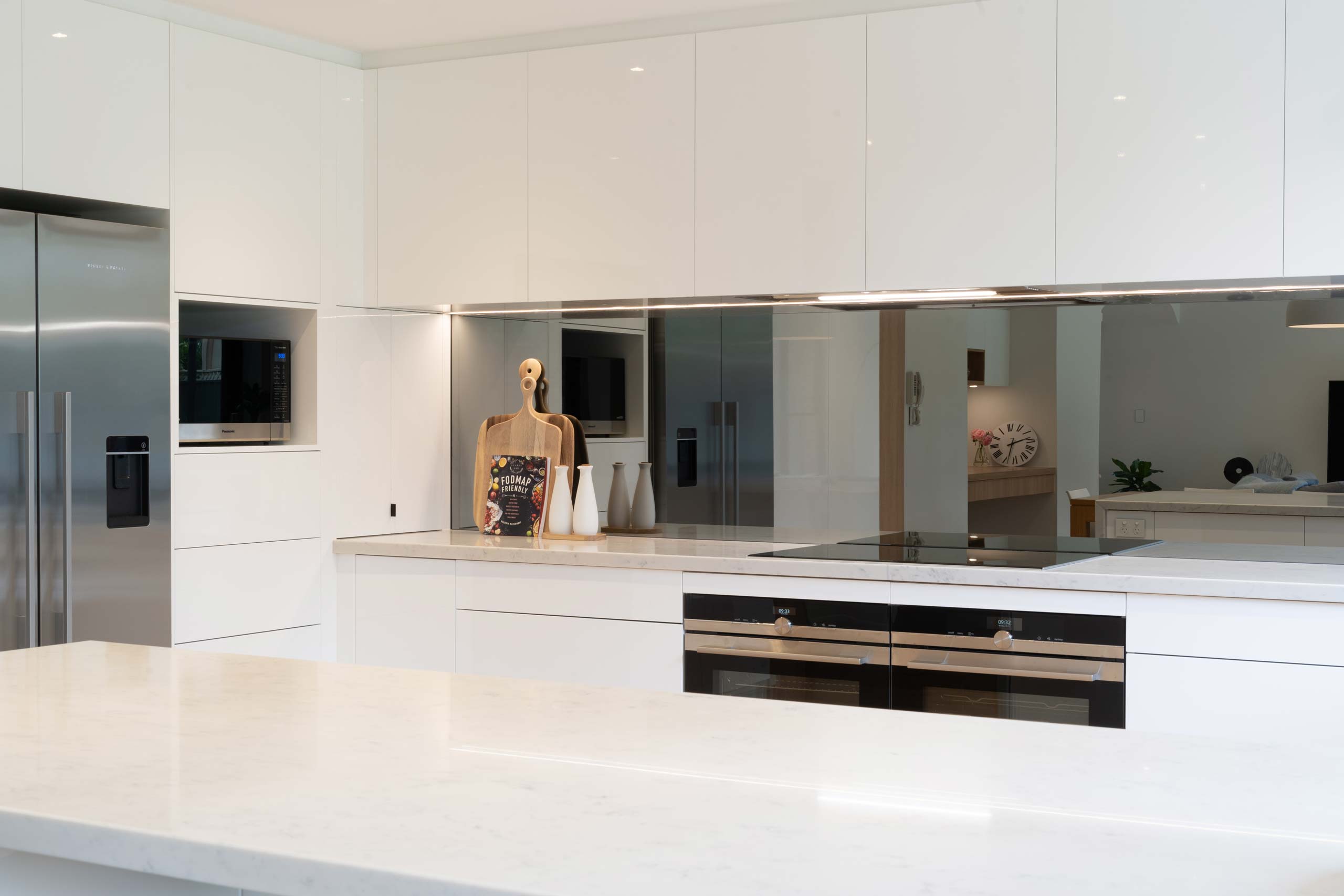 G shape open long white gloss kitchen. Large breakfast bar and seating area. mirrored splashback. Double ovens.