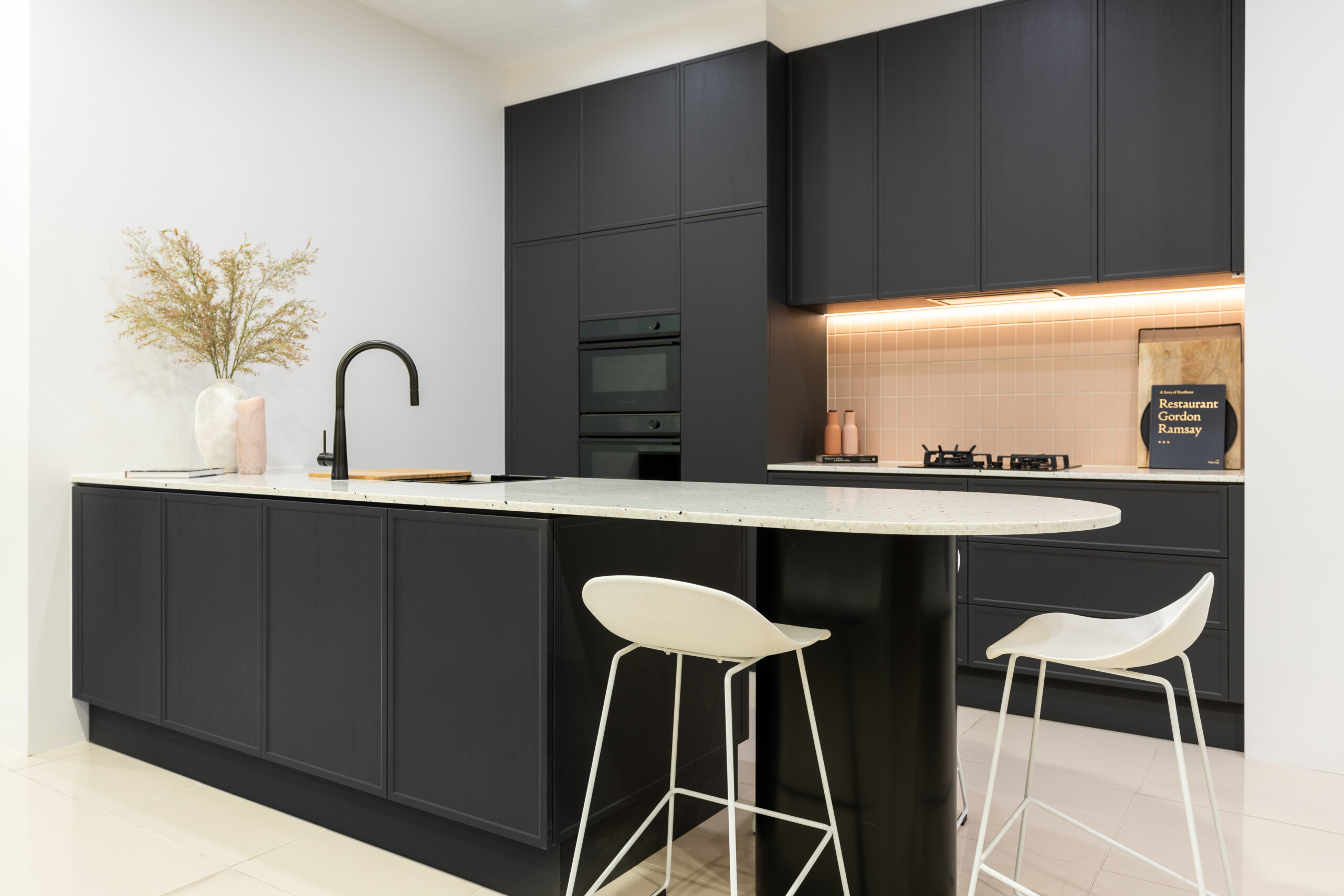 Graphite Paint flow Kiev 20 showroom kitchen. Curved benchtop in Sensa Siberia. Pink tiled splashback with black features throughout.