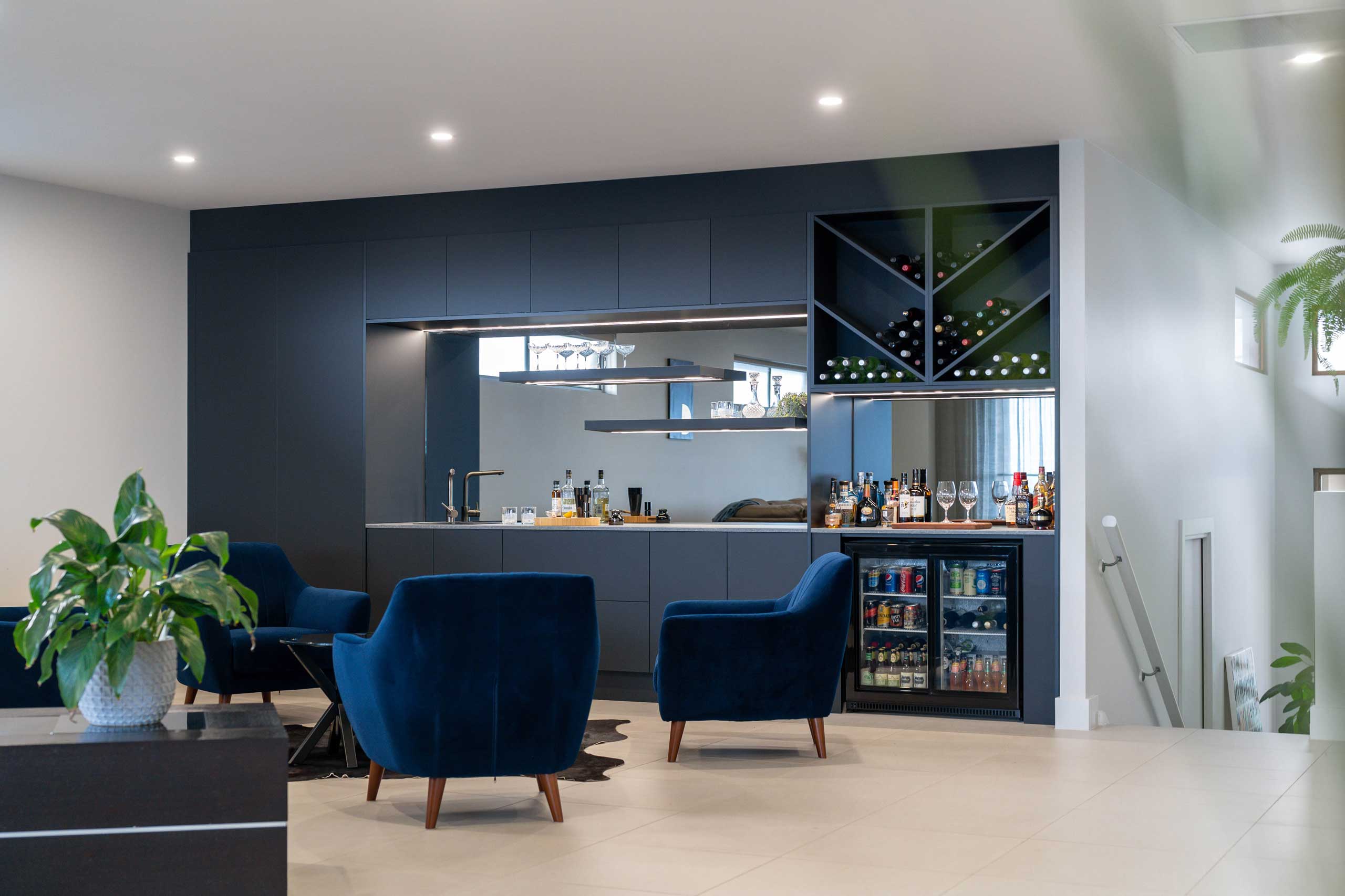 Open Bar space with diagonal wine racks and mirror feature. black touch cabinetry with stone serving benchtop.