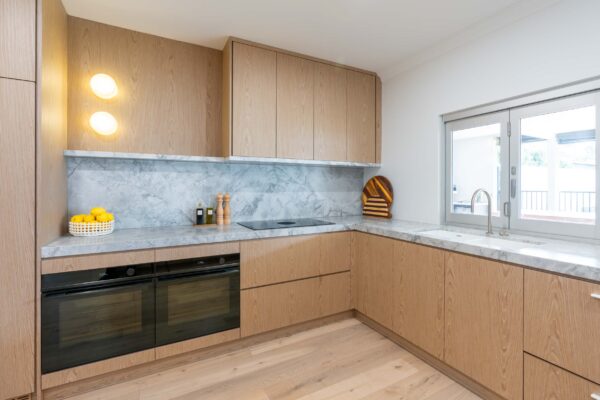 A soft palette kitchen. Light timbers and grey tone marble. Double ovens and open server window.