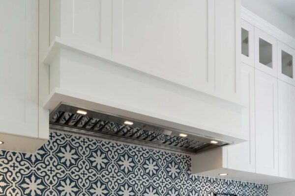 Rangehood. Overhead integrated with white Barossa cabinetry and glass insert panels. Navy and white patterned tiles.