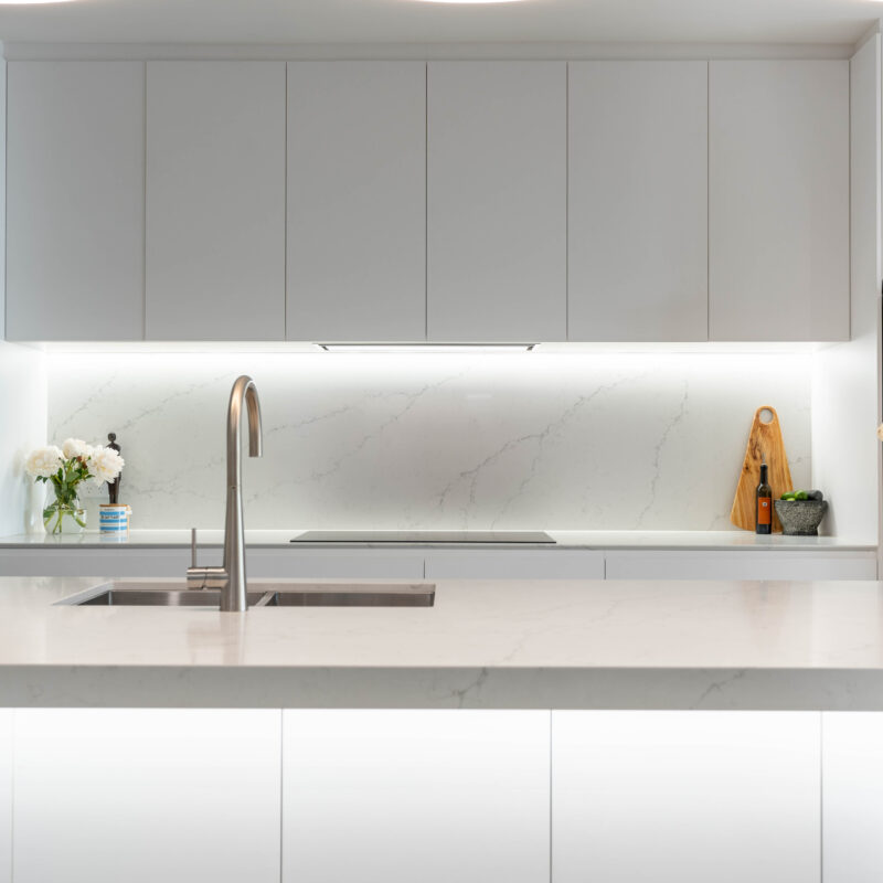 White classic slim line kitchen with curved led lighting and silver tap and sink. stone splashback.