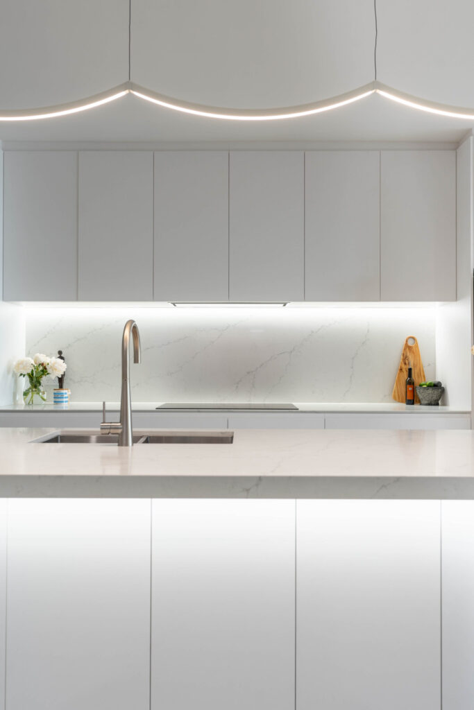 White classic slim line kitchen with curved led lighting and silver tap and sink. stone splashback.