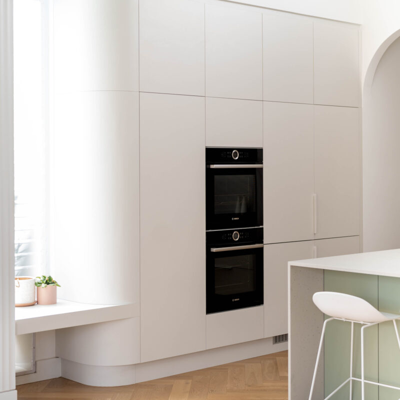 Kitchen. Calming curves. White grey curved cabinetry with oven wall and storage on a timber floor.