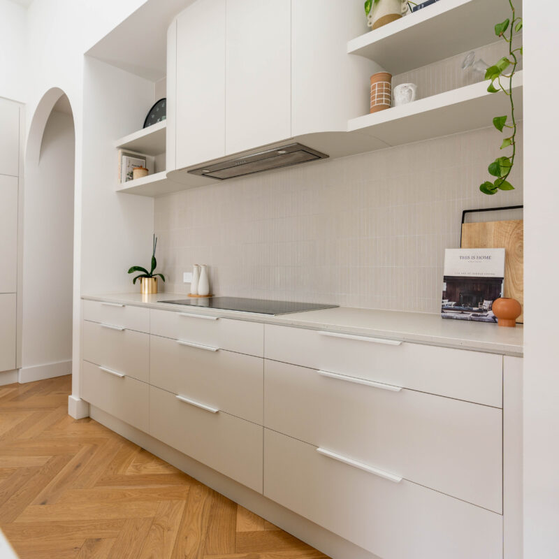 Kitchen back run of White grey cabinetry with curved rangehood and shelving with kit kat tiles. Calming curves.