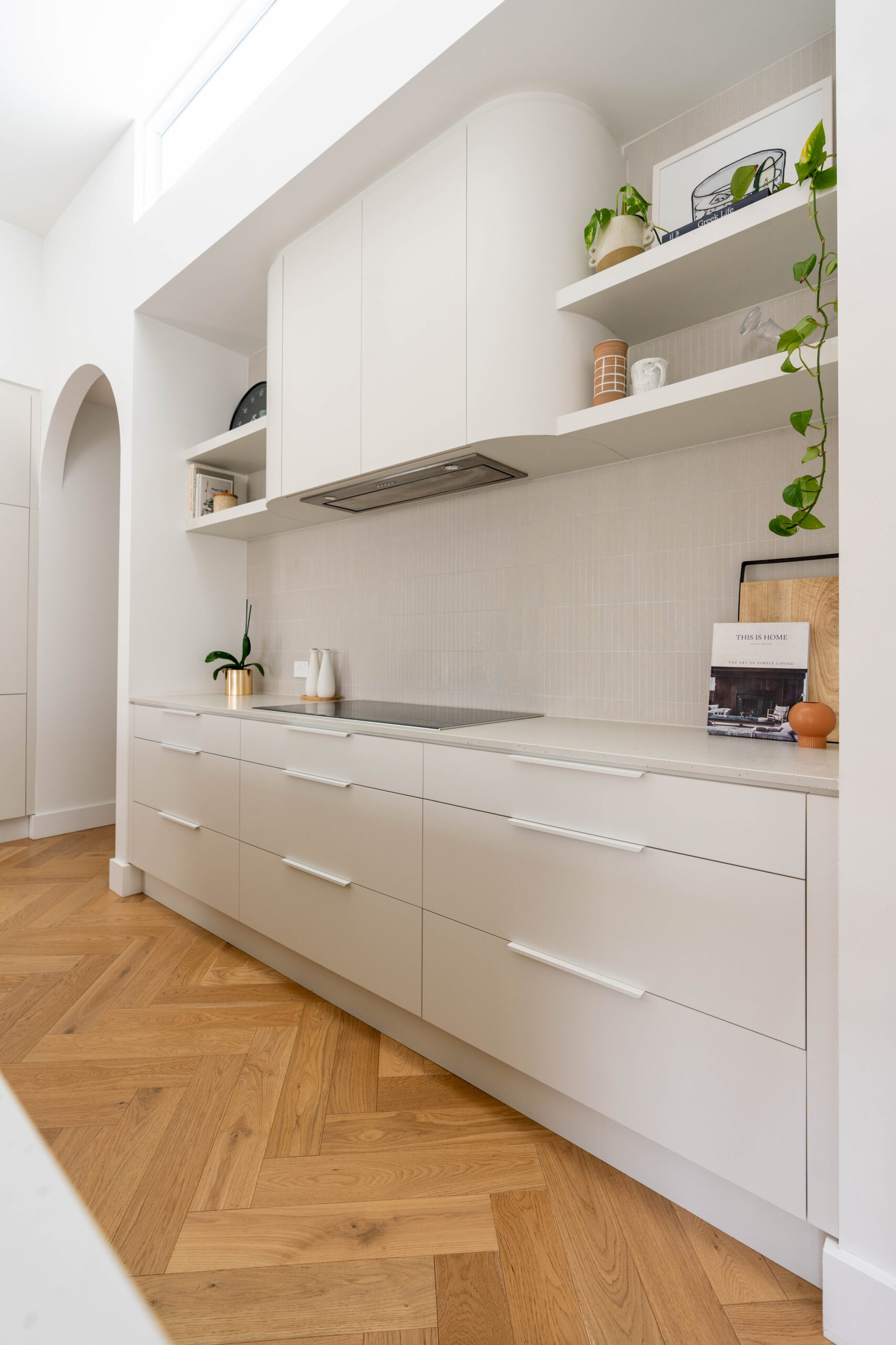 Kitchen back run of White grey cabinetry with curved rangehood and shelving with kit kat tiles. Calming curves.