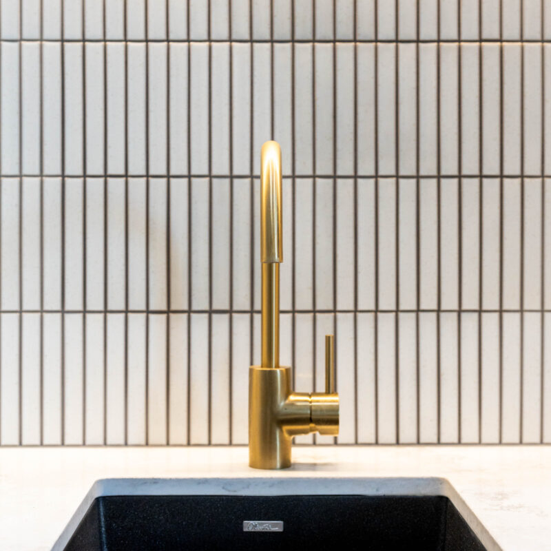 Gold tap and black Oliveri sink in laundry with kit kat tiles. Organic Minimalist.
