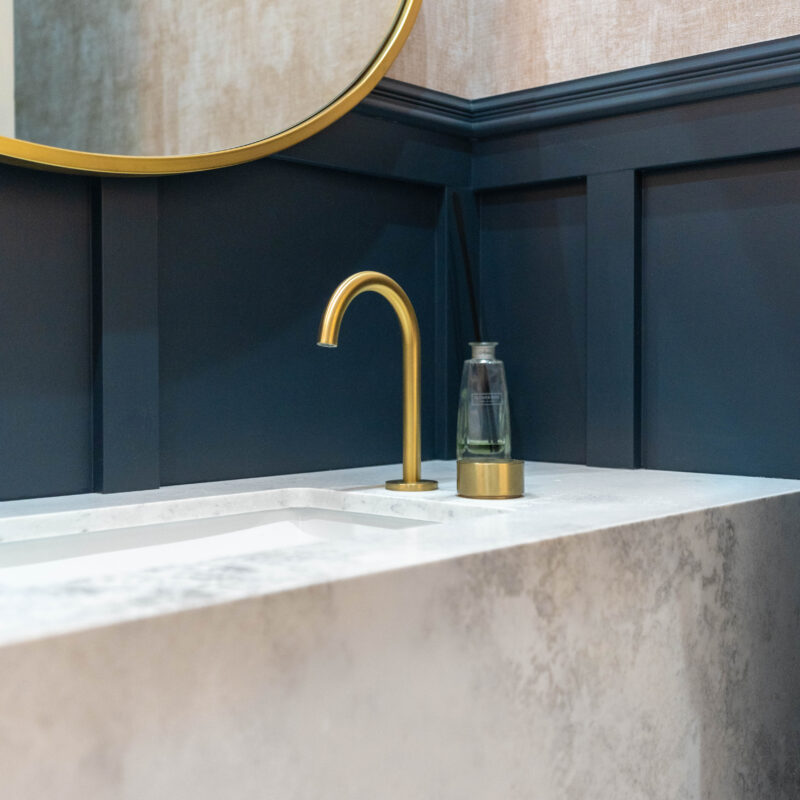 Bathroom vanity. Stone, marble look, traditional blue wall paneling and gold accents and mirror.
