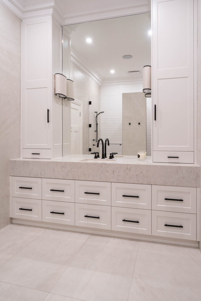 Elegant Bathroom with large vanity white cabinetry, black handles with large mirror and gorgeous side lights.