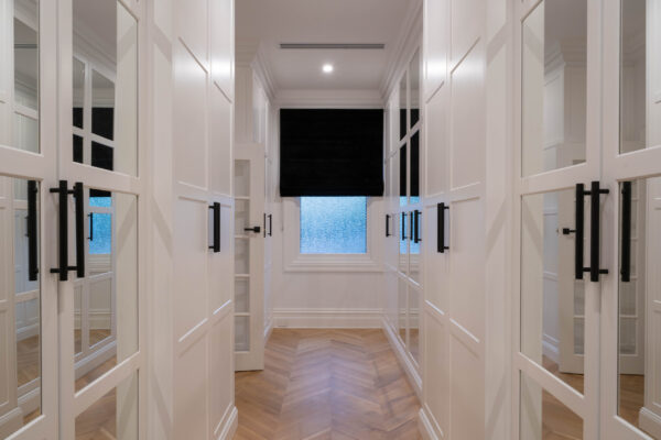 Walk in robe Hinged panels with black handles and mirrors in a light filled space.