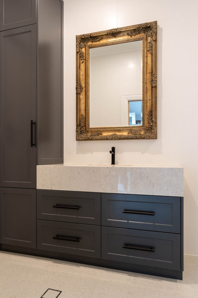 Bathroom Vanity. Barossa profile in a nice Graphite colour with deep warm stone like benchtop, black handles and gold filigree mirror.