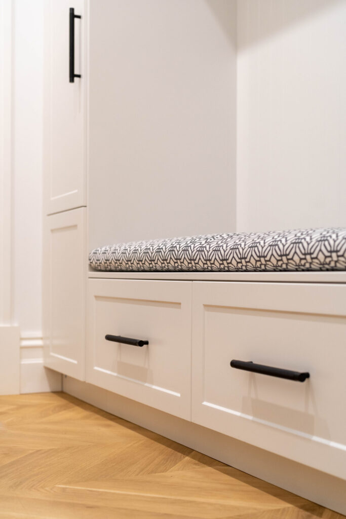 Cabinetry Detailing. The pearlescent finish of the cabinets in ghost gum satin swathes the space with the feel of luxury with bold, black metal accents and cushion in mud room seating area.