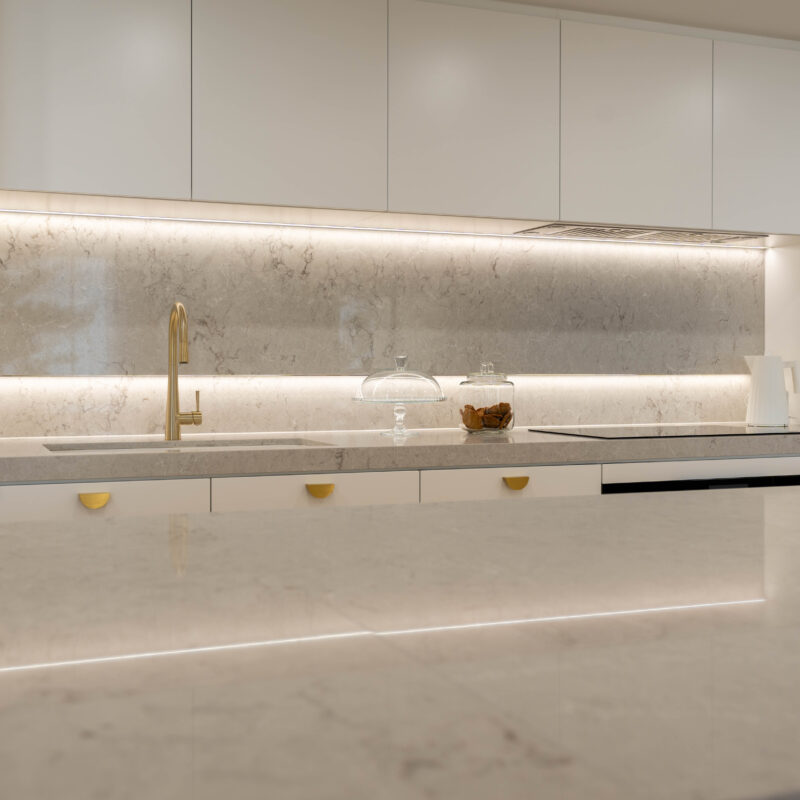 Illuminated Elegance Kitchen space. Open plan with herringbone light timber floors and curves. Premium white satin cabinetry with illuminated highlights with strip lighting and gold handles and tap with a soft beige stone.
