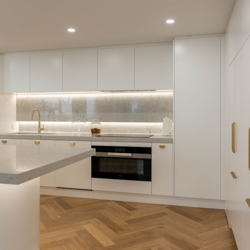 Illuminated Elegance Kitchen space. Open plan with herringbone light timber floors and curves. Premium white satin cabinetry with illuminated highlights with strip lighting and gold handles and tap.