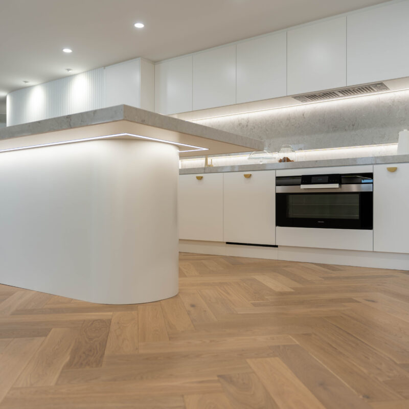 Illuminated Elegance Kitchen space. Open plan with herringbone light timber floors and curves. White and gold with illuminated highlights.