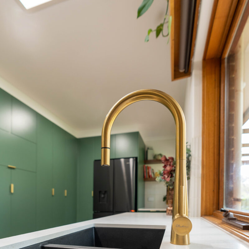 Gold Oliveri goose neck tap with gunmetal sink on white stone, in a hushed pine green kitchen.