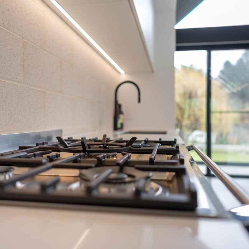 Black Fisher and Paykel freestanding oven and cooktop with black tap create a bold contrast with the run of white profile cabinetry.