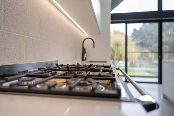 Black Fisher and Paykel freestanding oven and cooktop with black tap create a bold contrast with the run of white profile cabinetry.