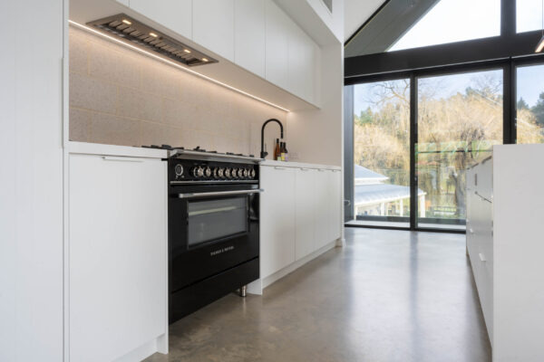 Black Fisher and Paykel freestanding oven and cooktop with black tap create a bold contrast with the run of white profile cabinetry.