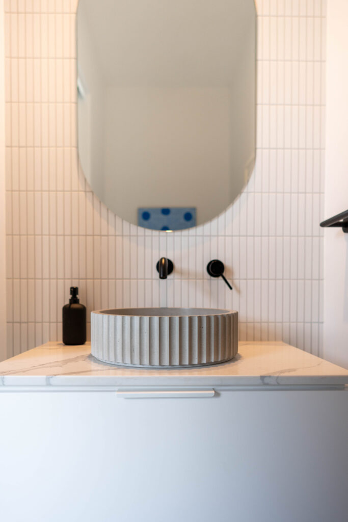 Small vanity with textured bowl and black tapware. Kit kat tiles and marble style stone benchtop.