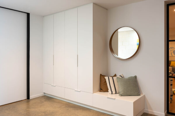 Beautiful white smooth cabinetry and white handles for mud room, seating space and storage. Mirror and cushions compliment the space.