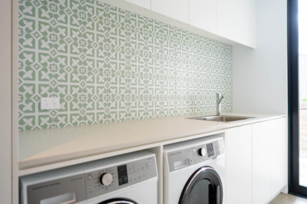 Laundry. White plain flat cabinetry with green pattern tiles and double space for washers.