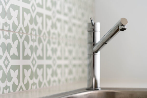 Laundry sink with chrome tap and green pattern splashback.