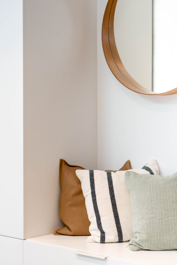 Small mud room seating nook, with round mirror and 3 natural cushions in different textures.