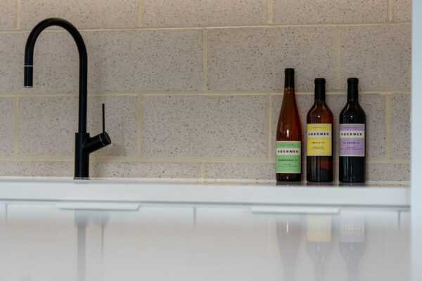 Breeze block splashback with black mixer tap and three Koerner wine bottles.