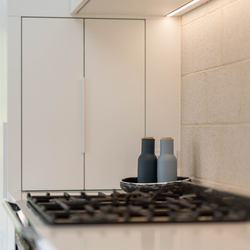 White cabinetry with natural breeze block splashback, cooktop and integrated rangehood and appliance nook.