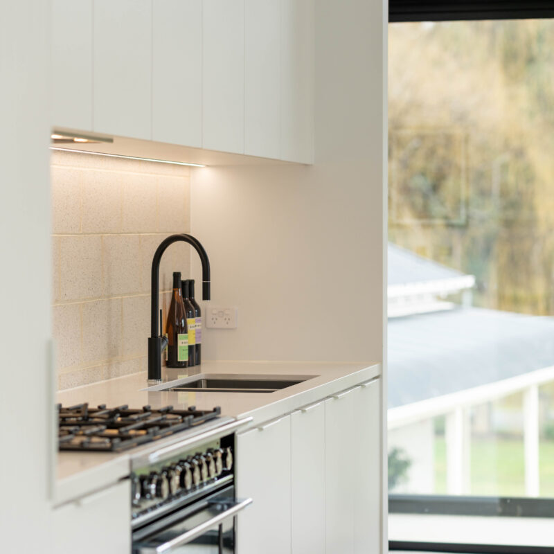 Black Fisher and Paykel freestanding oven and cooktop with black tap create a bold contrast with the run of white profile cabinetry.