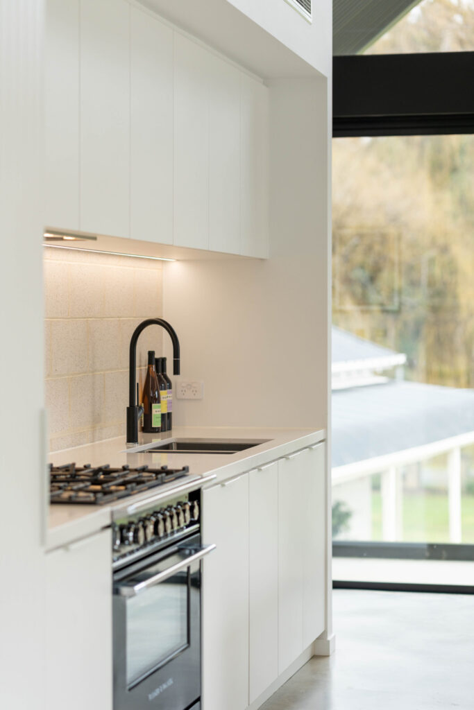 Black Fisher and Paykel freestanding oven and cooktop with black tap create a bold contrast with the run of white profile cabinetry.