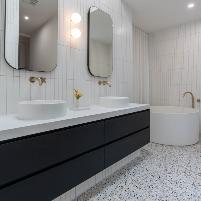 Family Bathroom space. Terrazzo floor and white vertical subway tiles. Double dark woodgrain vanity with gold accents.