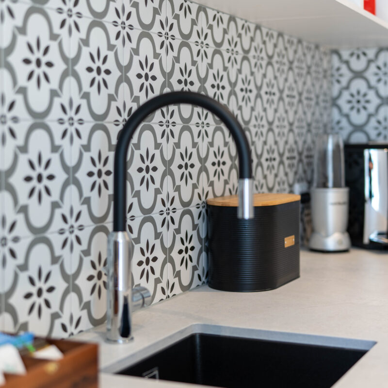Walk in pantry with patterned tile splashback in grey and black with black Oliveri tap and sink.