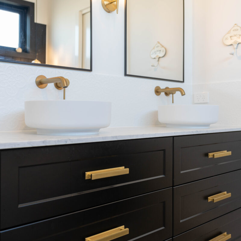 Bathroom Vanity- Double sink dark cabinetry with gold handles. Double mirrors and embossed white tiles.