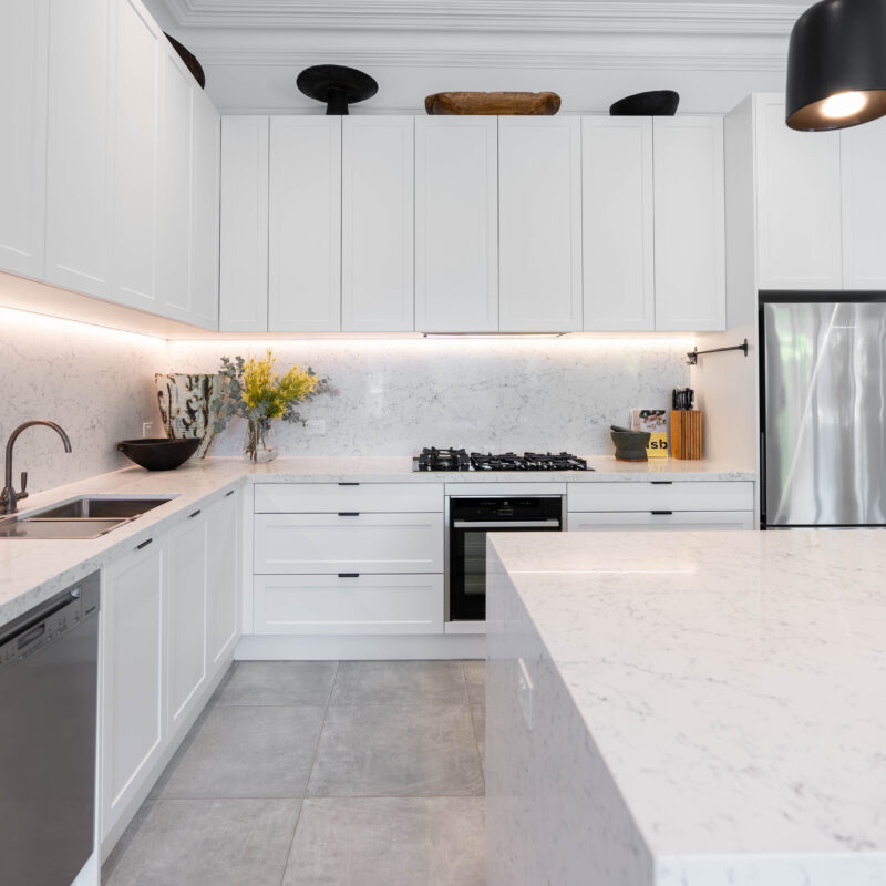 The splashback and benchtops feature an organic rush of grey tones, chosen to enhance the dark wooden artwork featured atop the meticulously designed cabinetry.