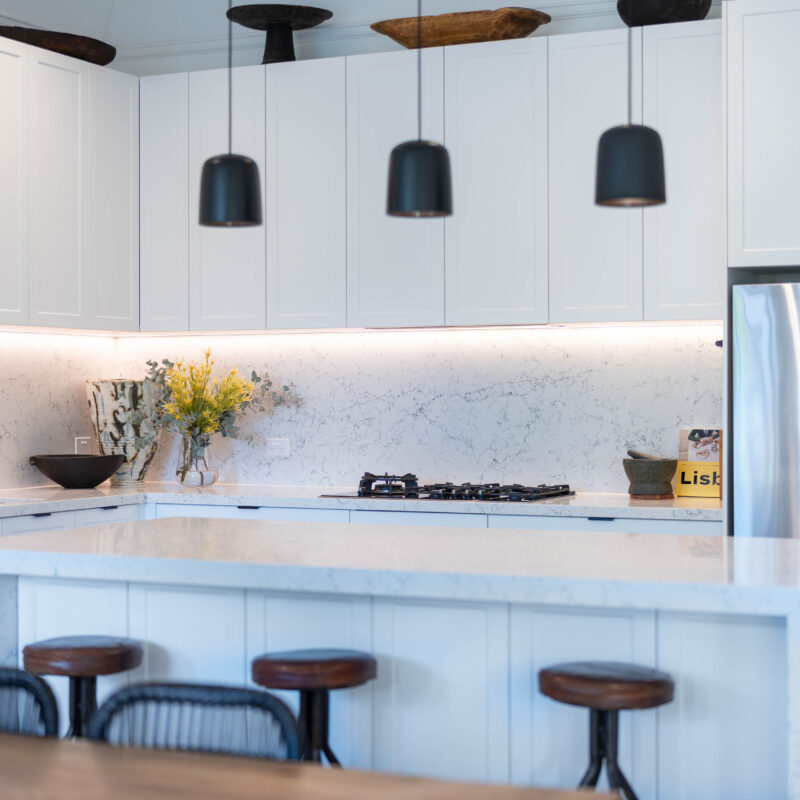 The splashback and benchtops feature an organic rush of grey tones, chosen to enhance the dark wooden artwork featured atop the meticulously designed cabinetry.
