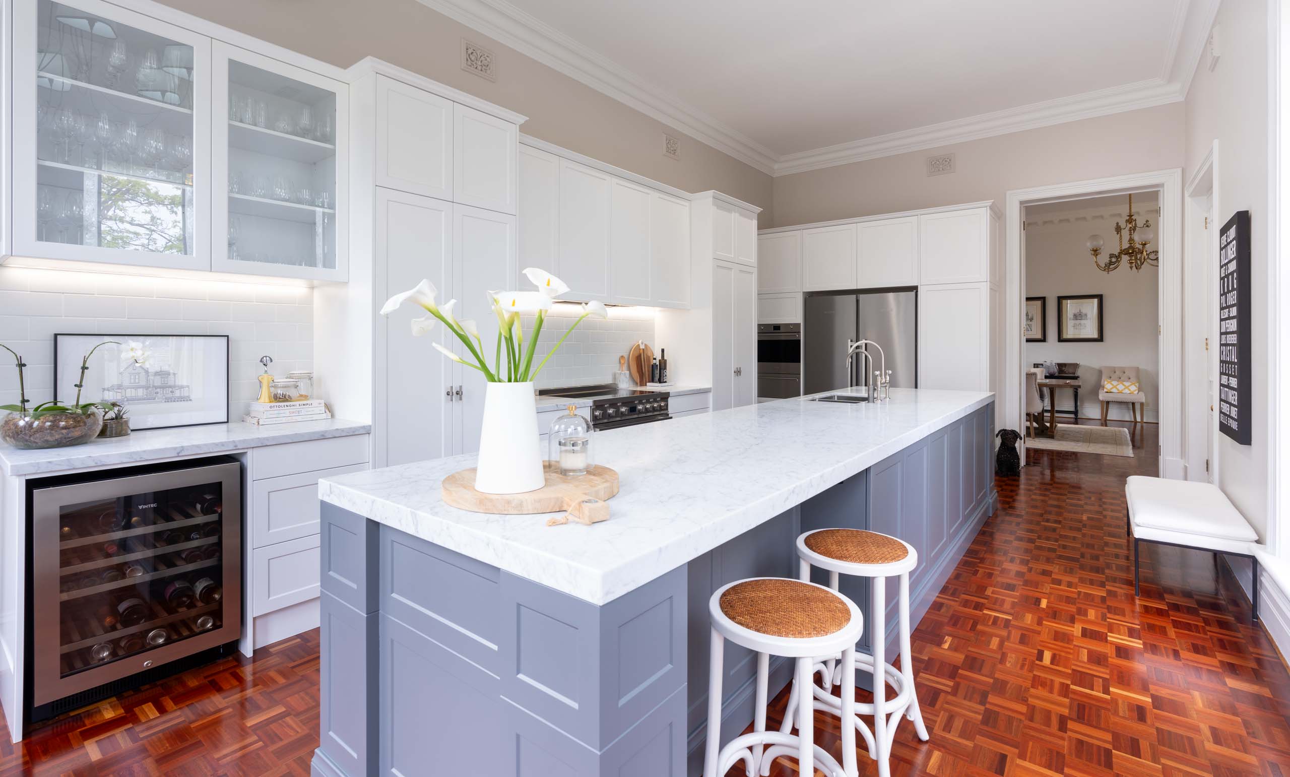The kitchen style is classic Hamptons - shaker profile cabinetry, Carrara marble benchtops, with a soft blue-grey vein against a white base, nickel hardware, and a freestanding cooker. White subway tiles keep the back run of the space light and uniform.