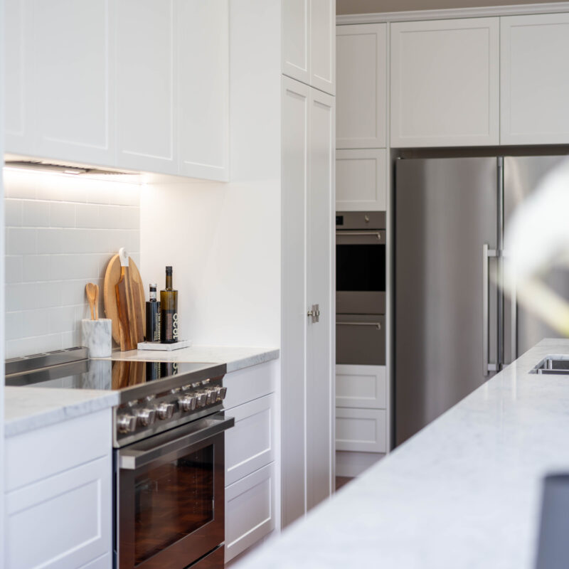 The kitchen style is classic Hamptons - shaker profile cabinetry, Carrara marble benchtops, with a soft blue-grey vein against a white base, nickel hardware, and a freestanding cooker. White subway tiles keep the back run of the space light and uniform. The Island The mid tone neutral grey of the island provides a depth of colour between the light and bright white cabinetry, and traditional warm toned parquetry. Entertainer's Delight The core kitchen space is balanced and mirror image. Extending down towards the windows, the kitchen transforms into an entertaining space; with a glass door cabinet, wine fridge, and space for four stools, mimicking a traditional table setting, with two either side.