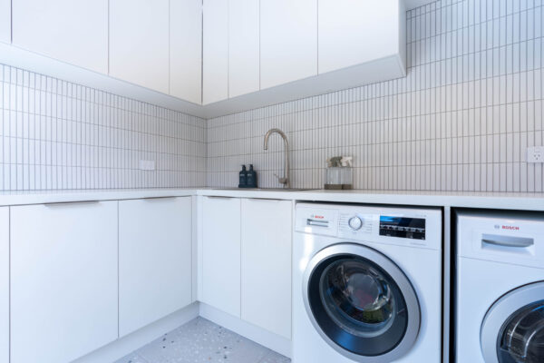 Laundry, L shaped. White cabinetry with laminate benchtop, Overheads and double washing machines.