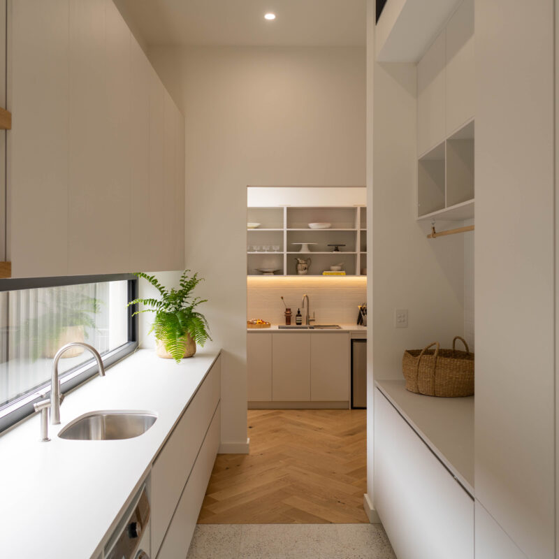 Walk in pantry storage and laundry space all connected together. White, light and bright with warm and natural tones and window glass splashback to let the light in.