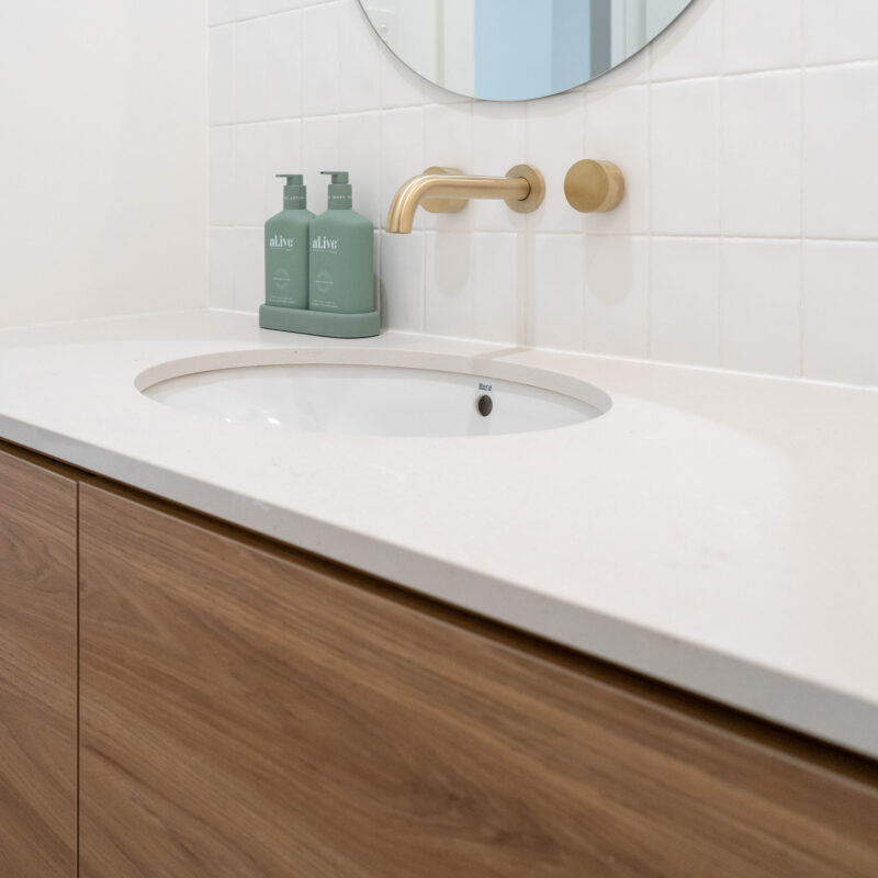 Beautiful bathroom longline drawer vanity in walnut and large oval mirror and gold wall taps.